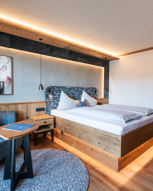 Moderna camera d'hotel con pavimento in legno, letto grande, divano blu e illuminazione calda